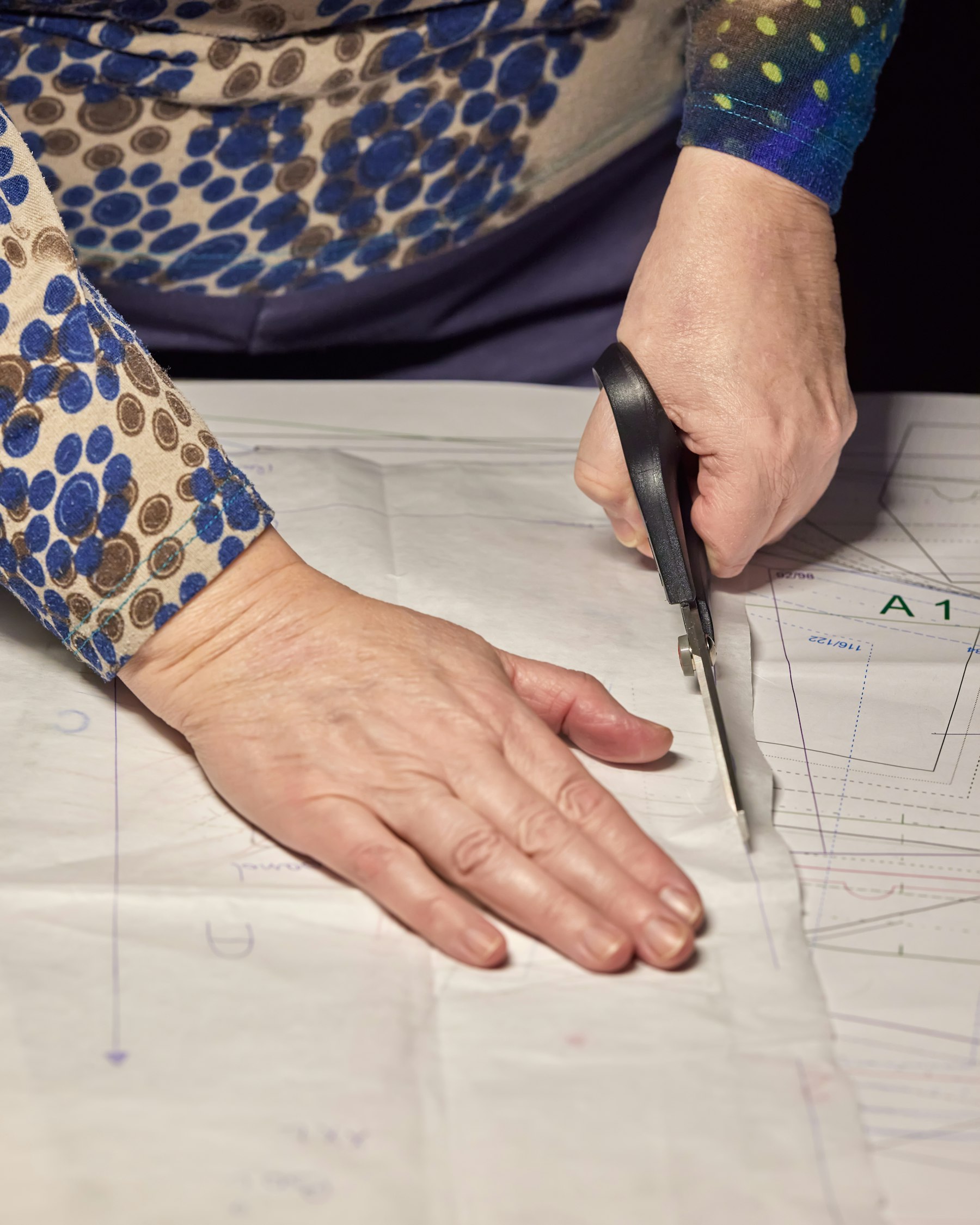 Hands cutting a paper sewing pattern with scissors